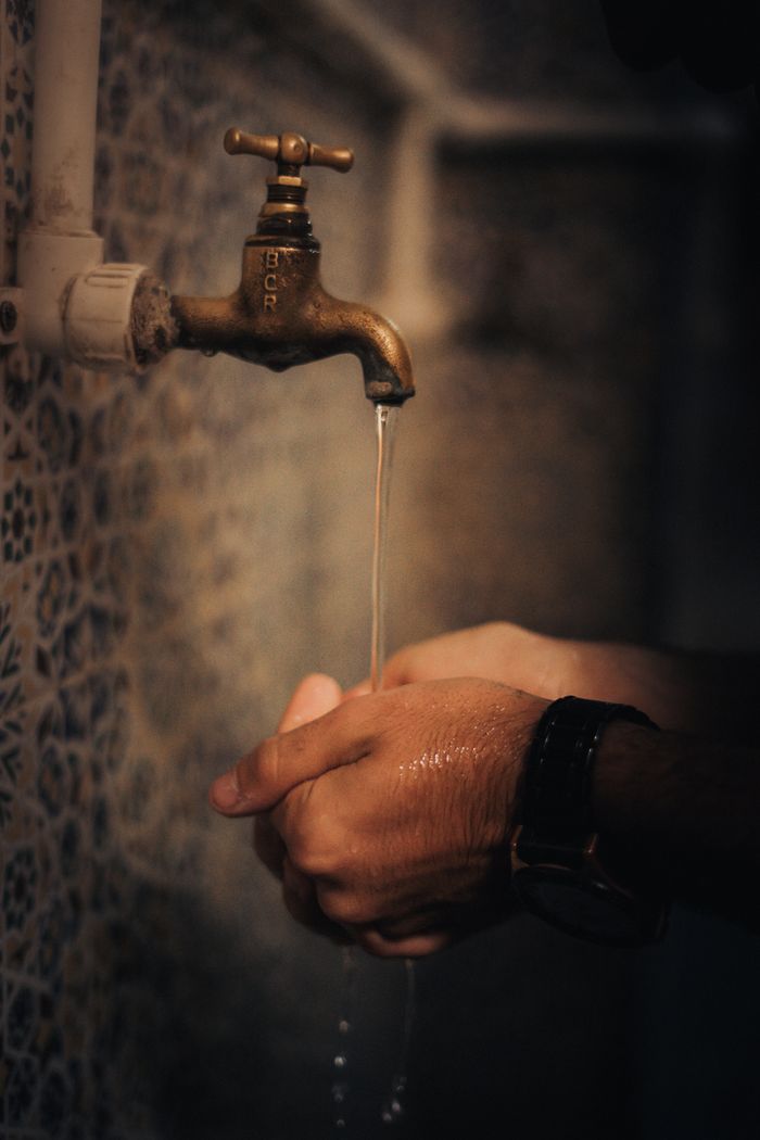 Close-up of hands washing under a vintage tap with water dripping in a dimly lit space.